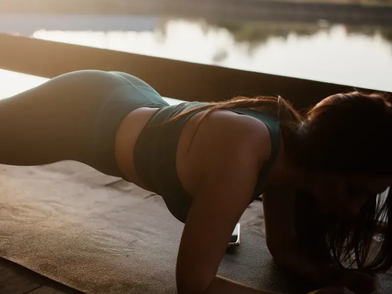 A woman holding a plank on a wooden lakeside deck at sunrise