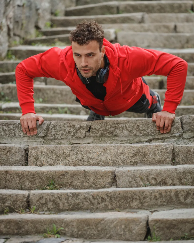 A man in a red hoodie doing push-ups on a flight of stone steps