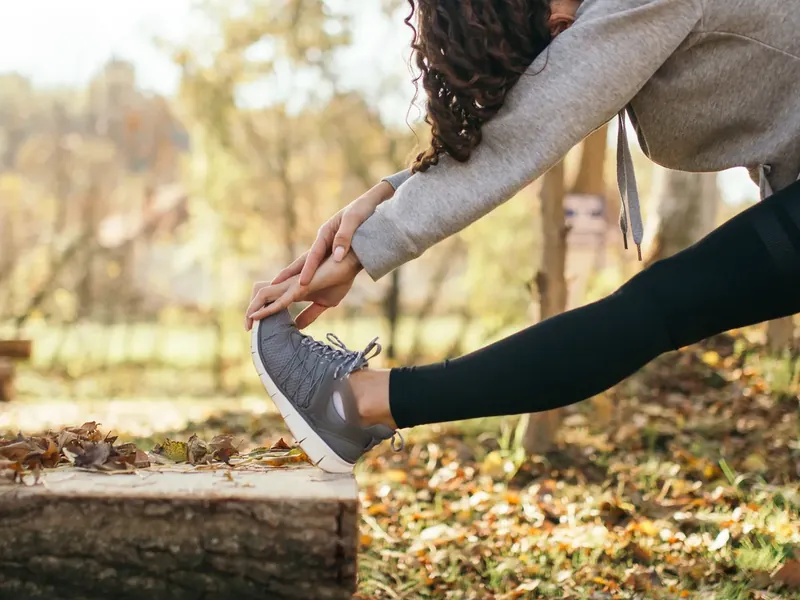 A woman stretching a hamstring with her foot on a low wall